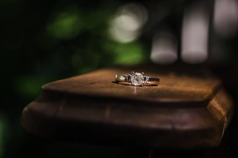 Close-up of a diamond ring resting on a wooden surface with a blurred green background.
