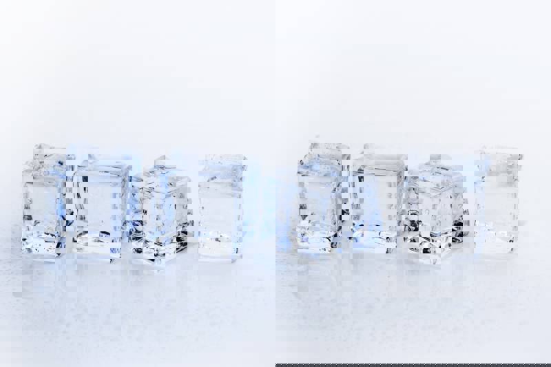 Four clear ice cubes on a reflective surface with droplets of water.