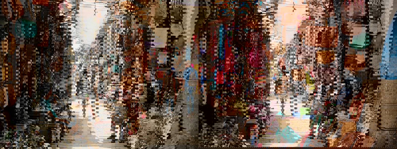 Busy market street lined with colourful bags and handmade crafts.