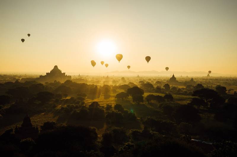 Hot air balloons over a misty landscape at sunrise, with ancient temples in the background.