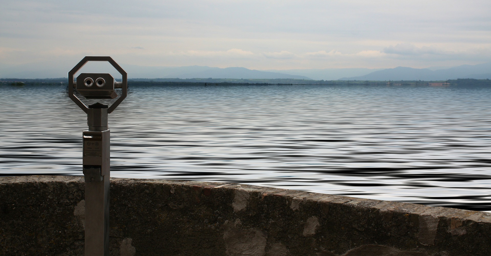 Viewing telescope overlooking a calm lake with distant mountains in the background.