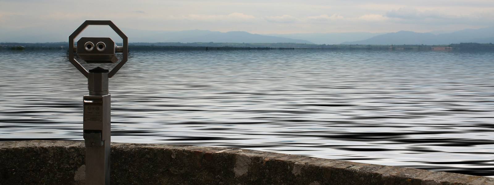 Viewing telescope overlooking a calm lake with distant mountains in the background.