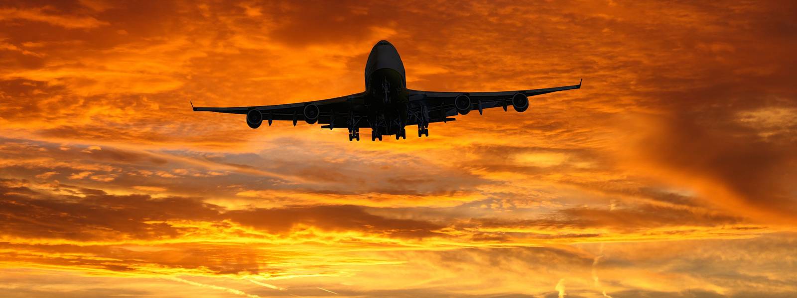 Silhouette of an airplane flying against a vibrant orange sunset sky.