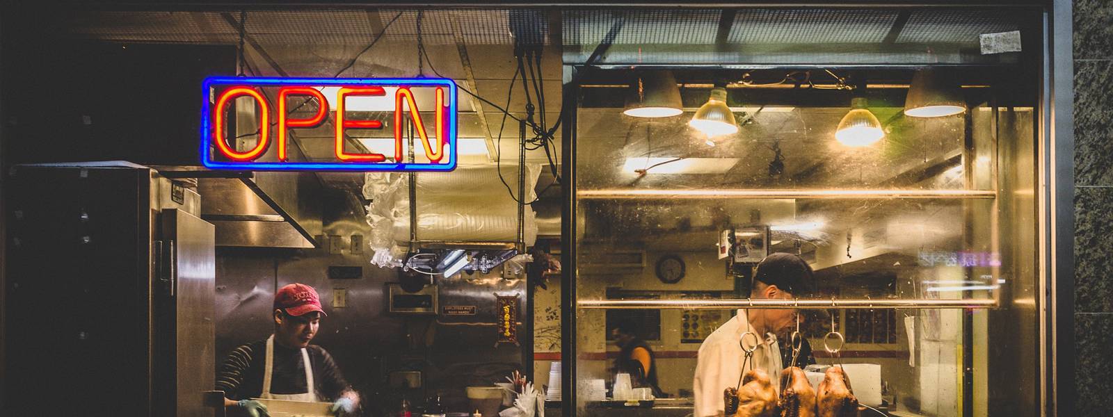 Two chefs working in a restaurant kitchen with an illuminated 'OPEN' sign.