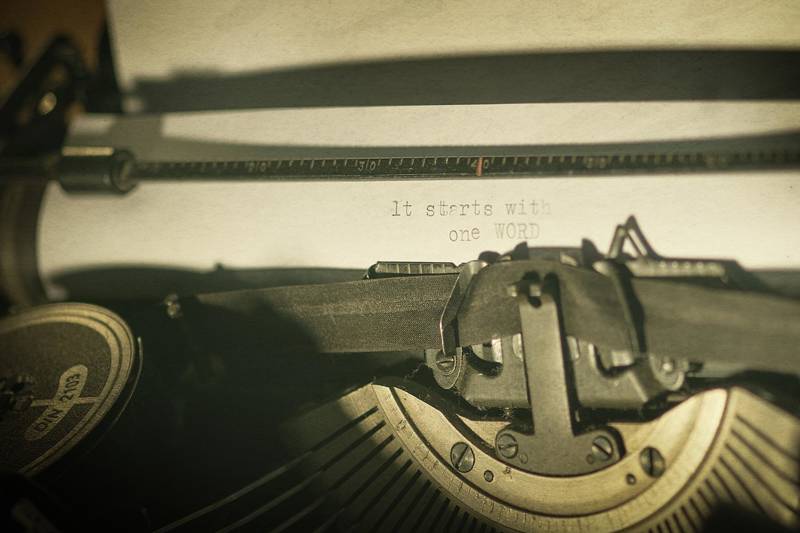 Close-up of a typewriter with the text 'It starts with one WORD' on paper.