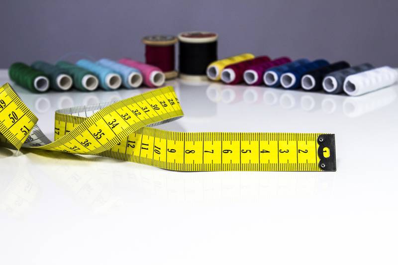 Close-up of a tailors yellow measuring tape with colourful thread spools arranged behind it.
