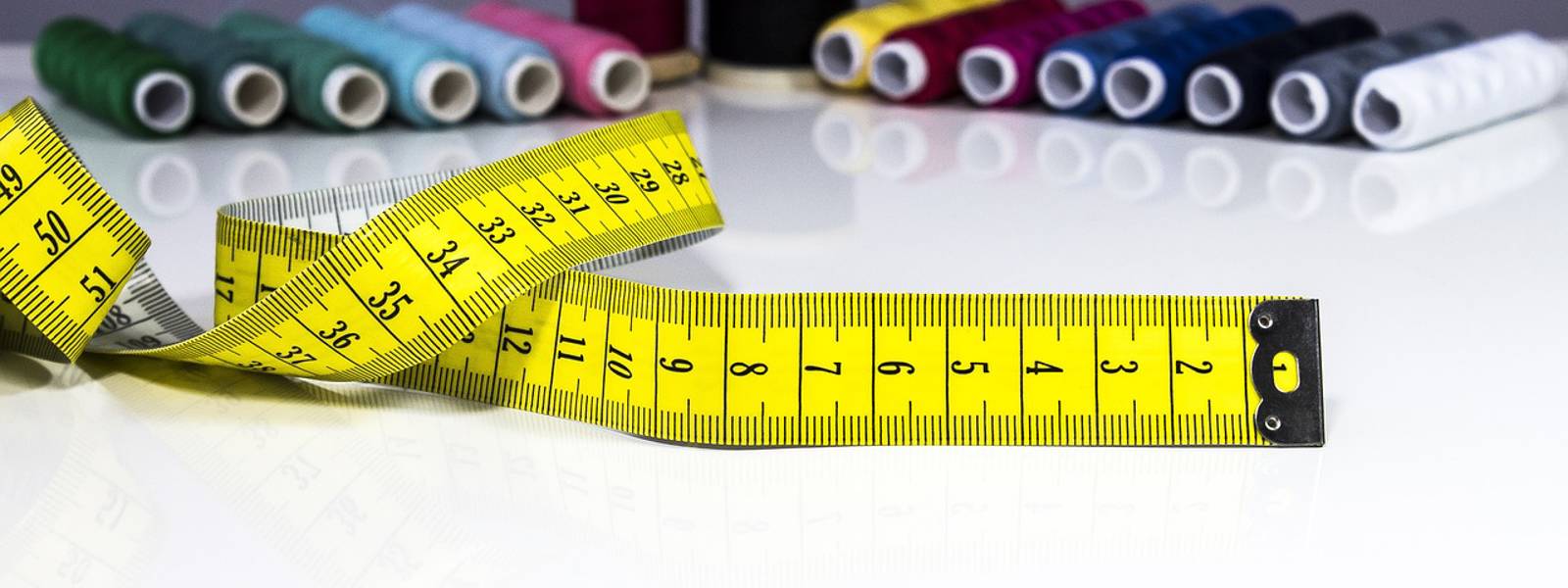 Close-up of a tailors yellow measuring tape with colourful thread spools arranged behind it.