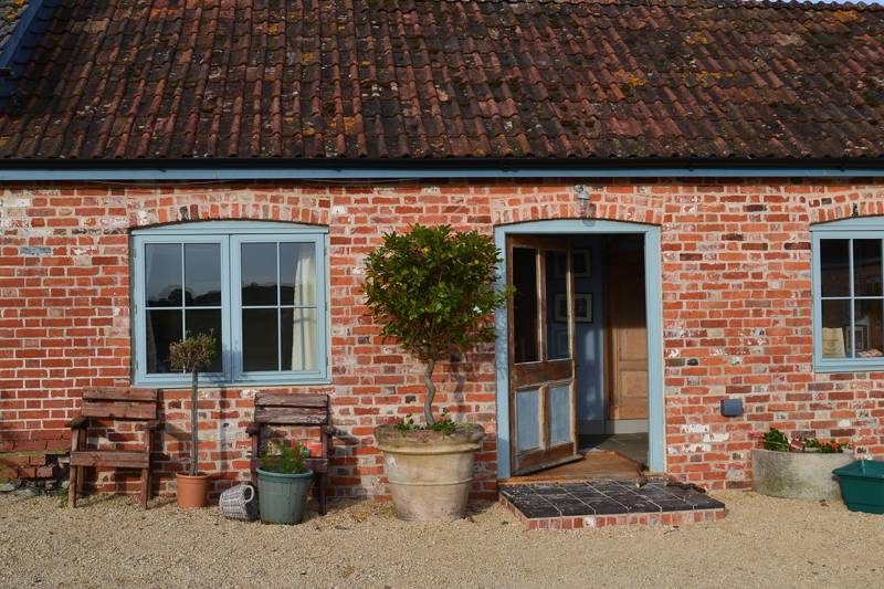Charming brick cottage entrance with potted plants and wooden benches.