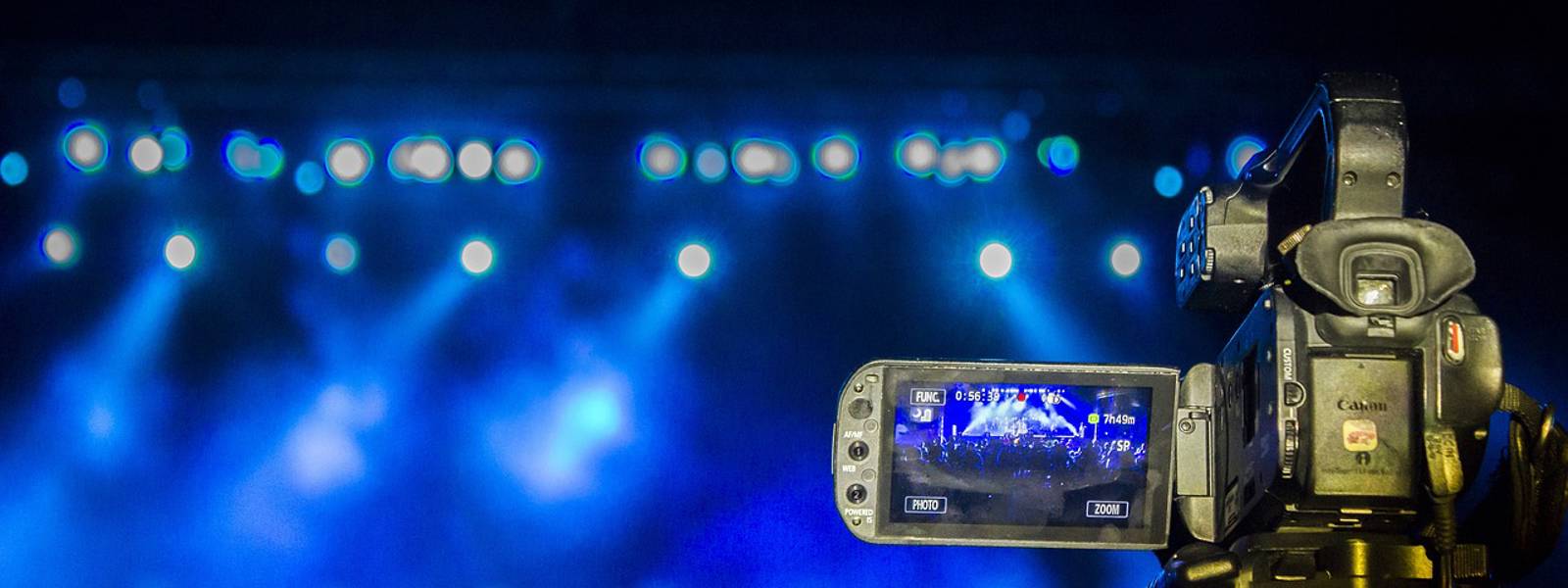 Video camera focused on a concert stage illuminated by blue lighting.